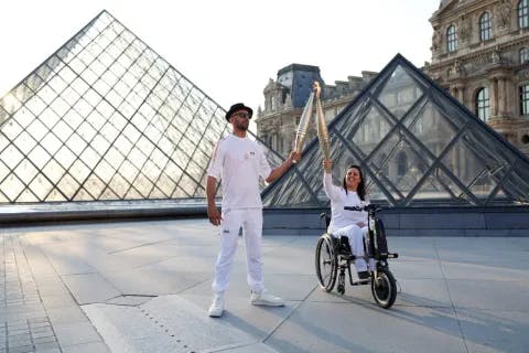 Bearers of the flame JR, French photographer and street artist, and Sandra Laoura, French skier, pass the Olympic flame on July 14, 2024, at the Louvre in Paris, France.
